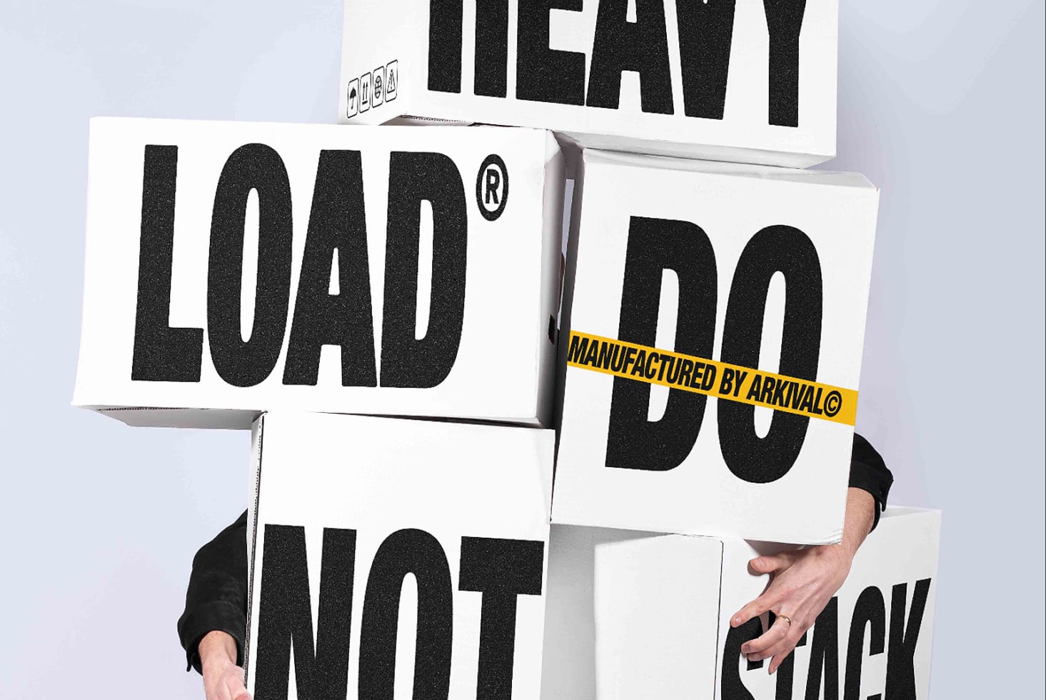 Person holding stacked boxes with bold black typography, yellow warning tape across middle box