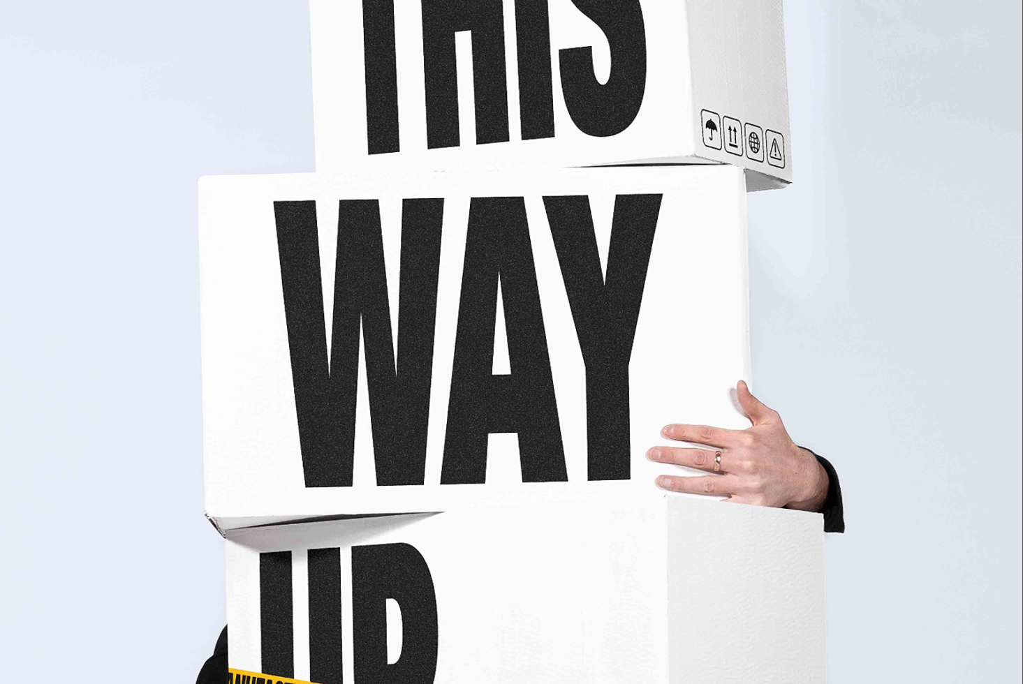 Person holding stacked white boxes with bold black typography saying "this way up"