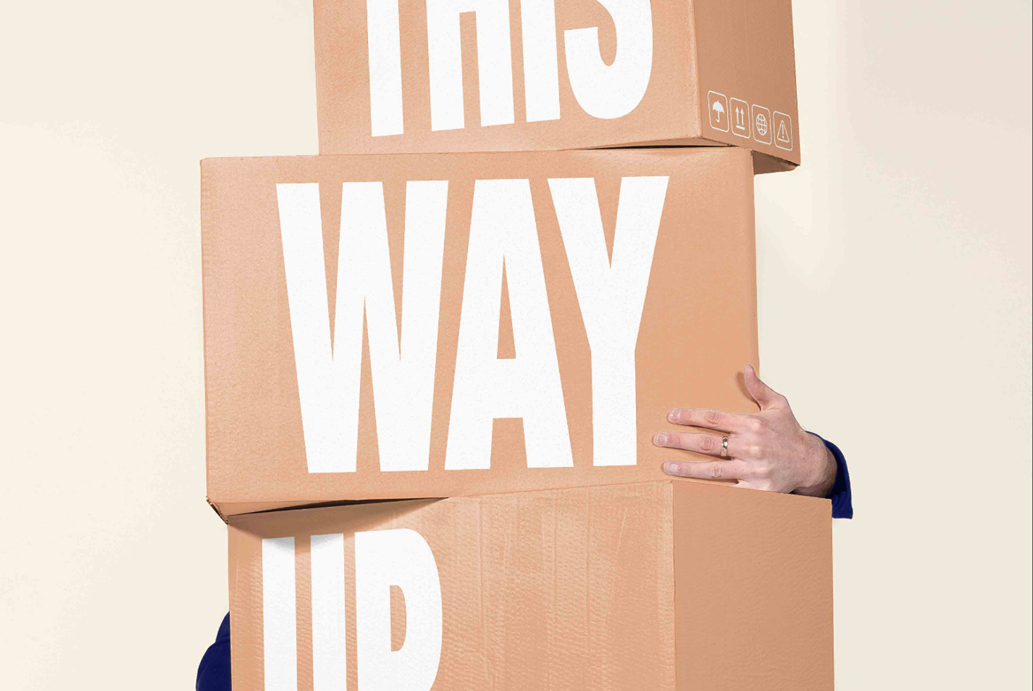 Stacked cardboard boxes with cutout lettering spelling "this way up" held by person's hand