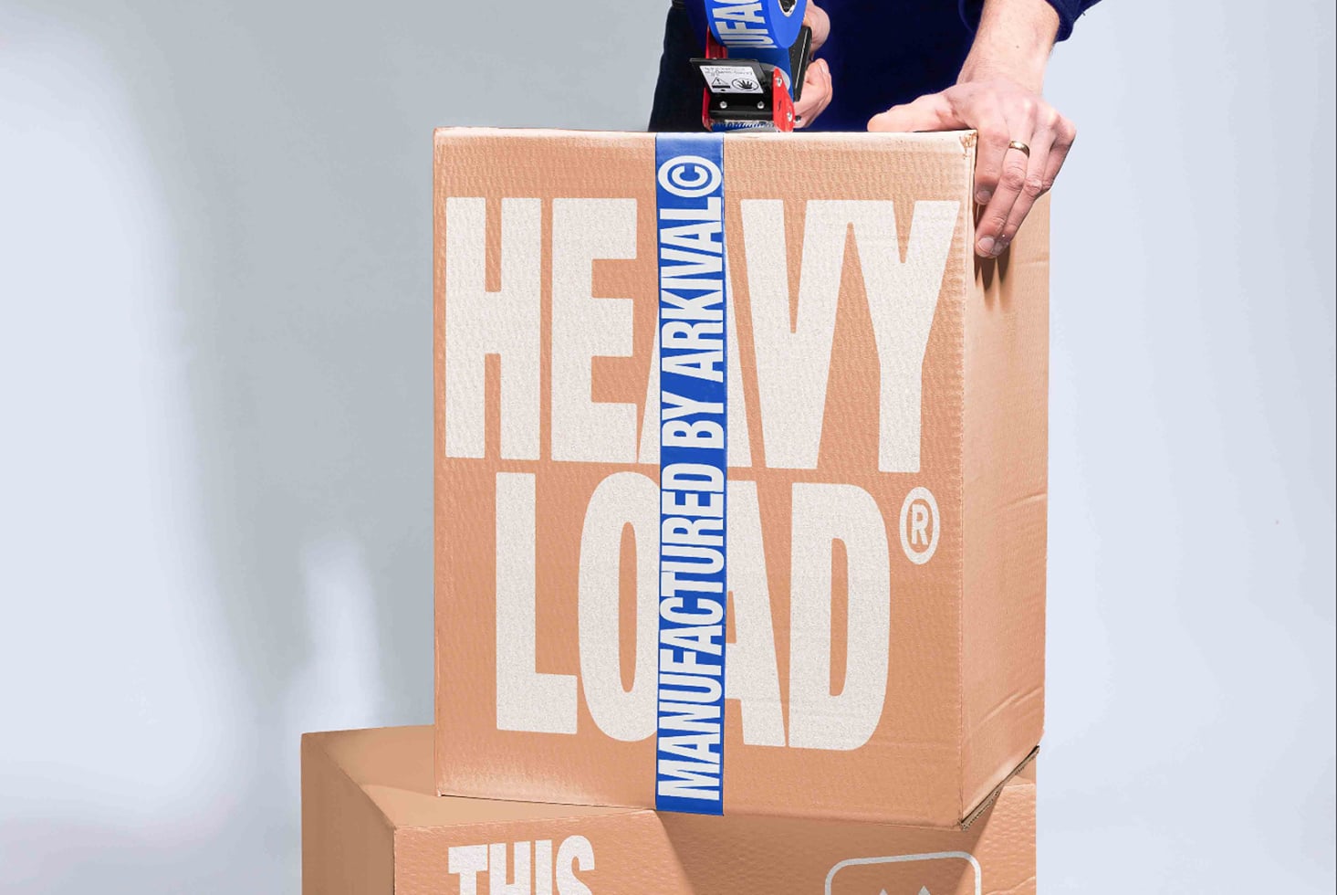 Hands holding cardboard box with "NEW LOAD" text plus blue manufacturer tape across it