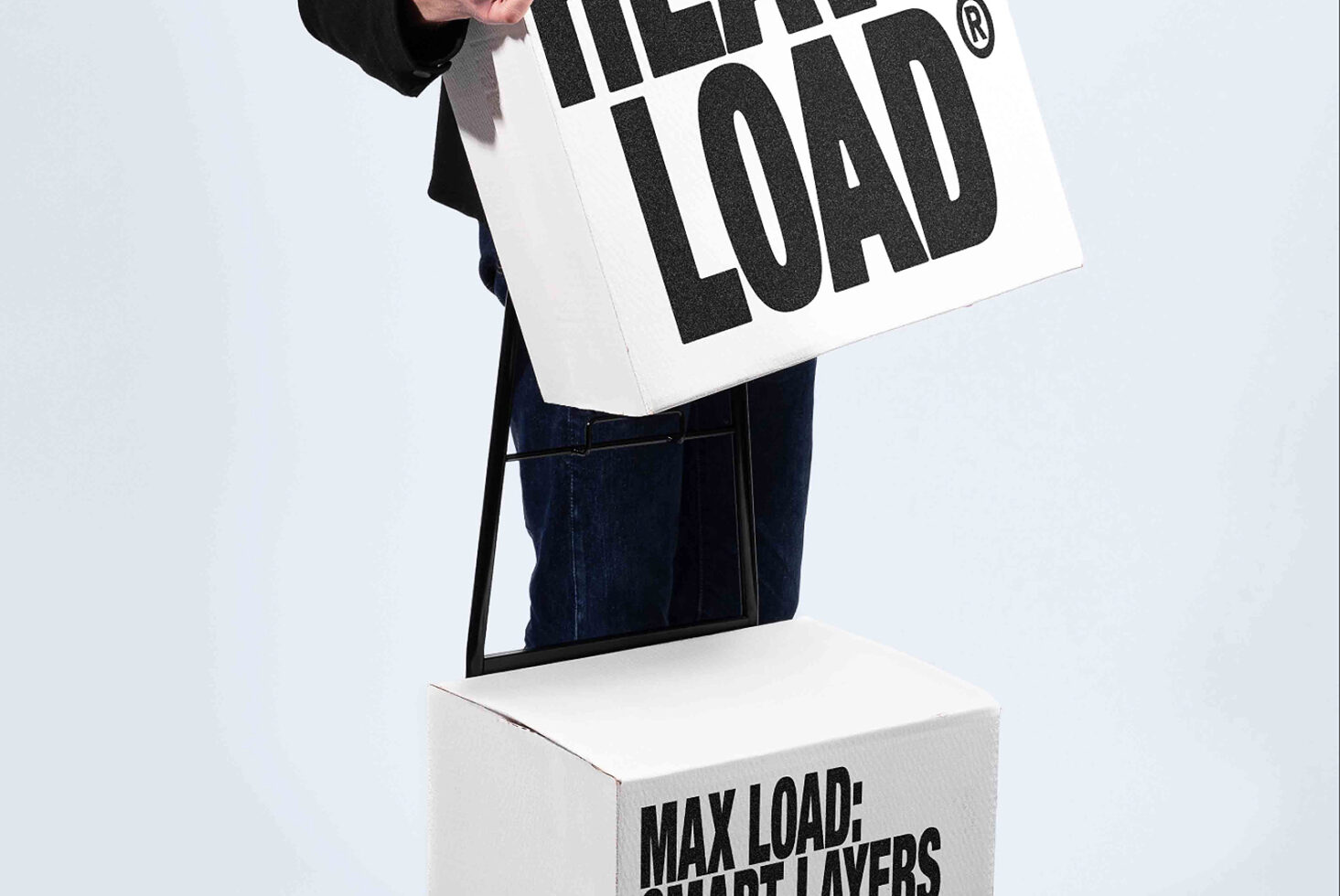 Hand holding white tote bag with bold black "LOAD" text over white box labeled "MAX LOAD"