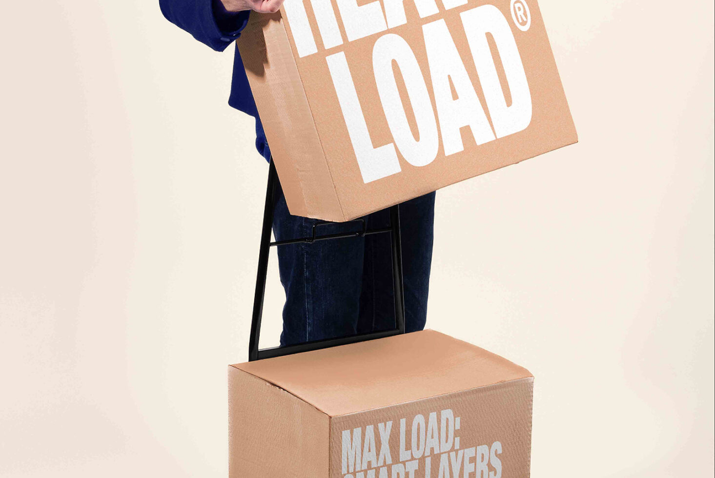 Person holding kraft cardboard box with white bold text, stacked boxes below showing product branding