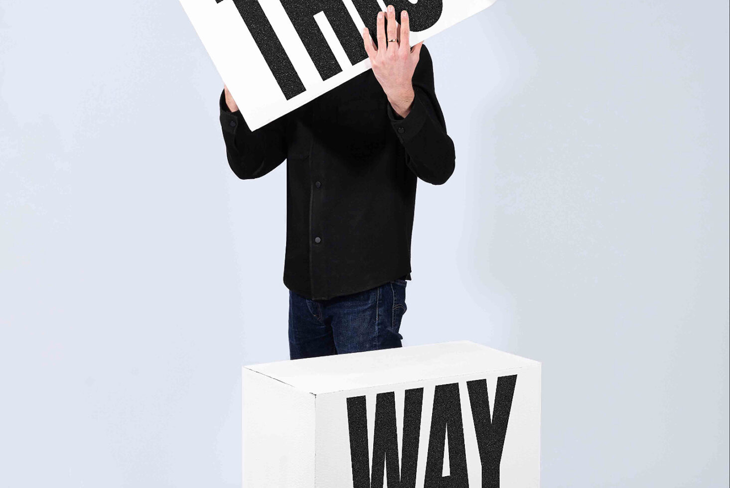 Person in black blazer holding white board with bold black stripes above box with WAV text
