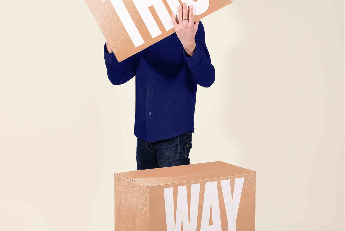 Person in navy shirt holding striped poster board above cardboard box with WAY text