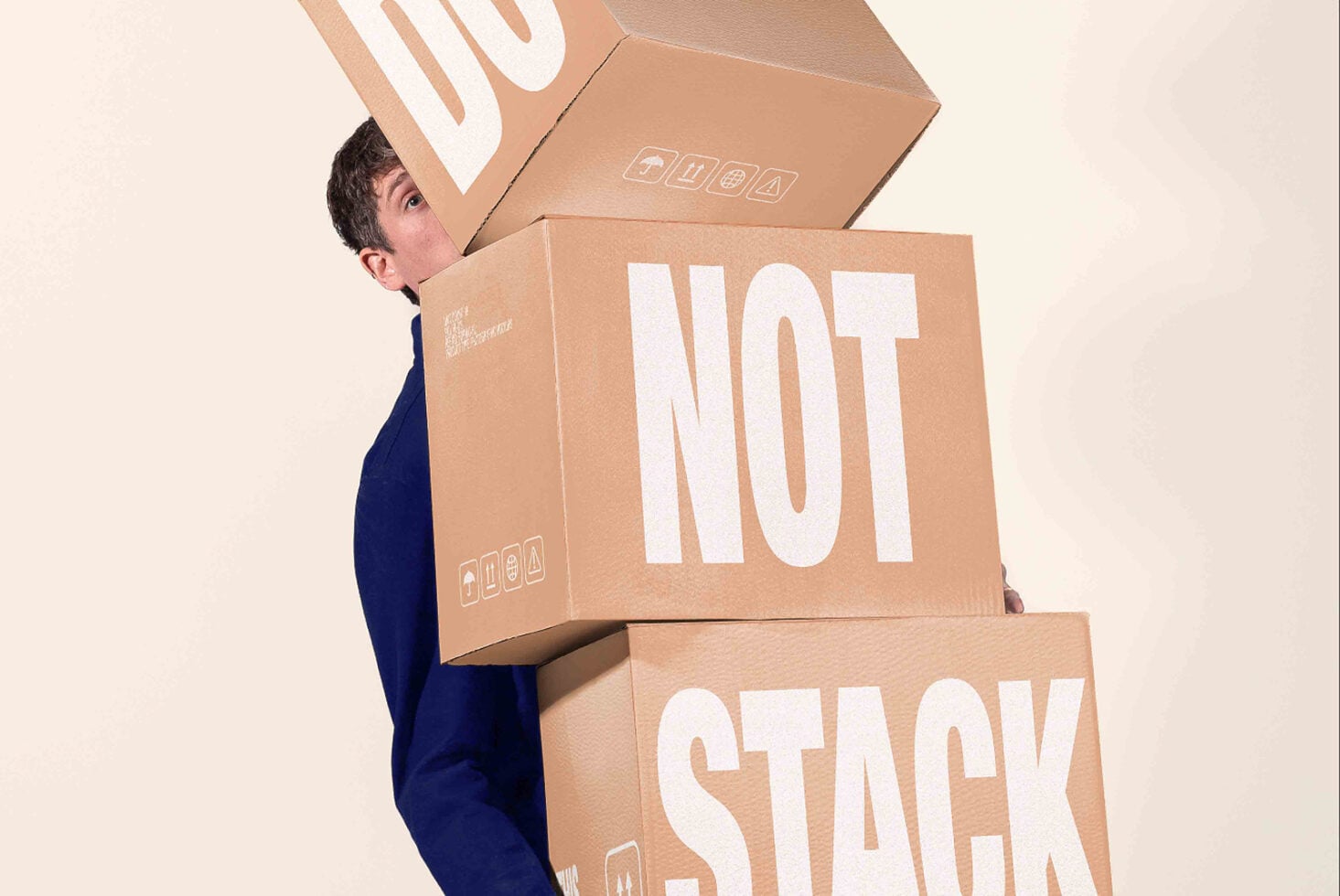 Guy balancing cardboard boxes stacked with "NOT STACK" text printed on them