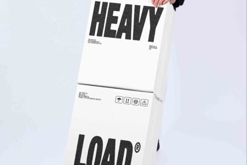 Cardboard box mockup with bold sans serif typography showing "HEAVY" on top, shipping symbols, handling labels, being held by hand against neutral background