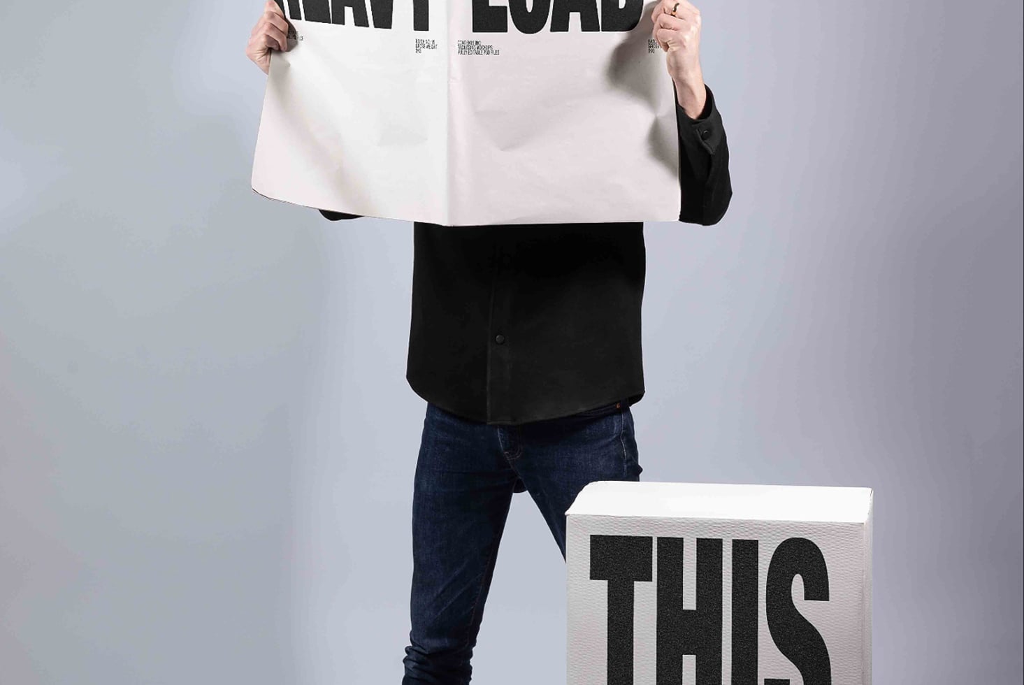 Person holding large white poster mockup with bold typography, smaller cube mockup below