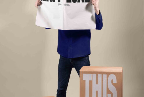 Person holding white tee mockup above head with wooden box displaying "THIS" text below