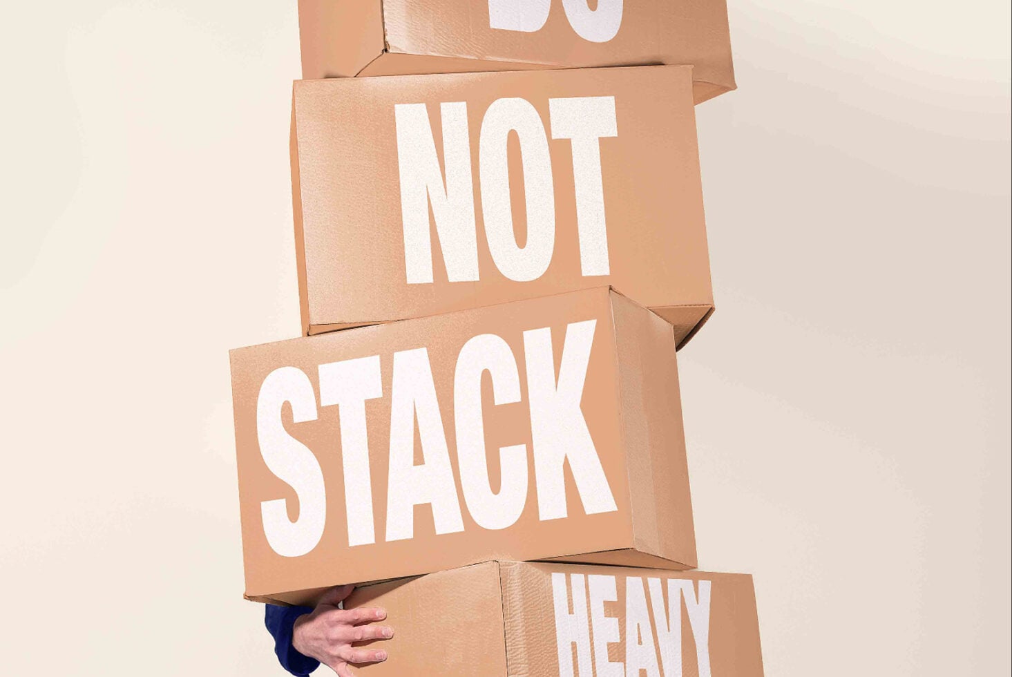 Stacked cardboard boxes with white text reading "NOT STACK HEAVY" held by person's hands