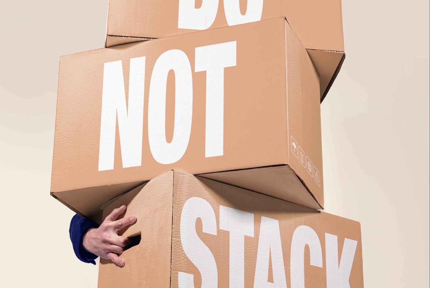Stacked cardboard boxes with "NOT" plus "STACK" text, hand visible holding bottom box