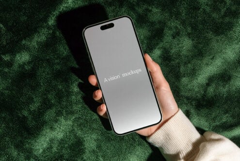 Hand holding modern smartphone with blank screen on textured green fabric background