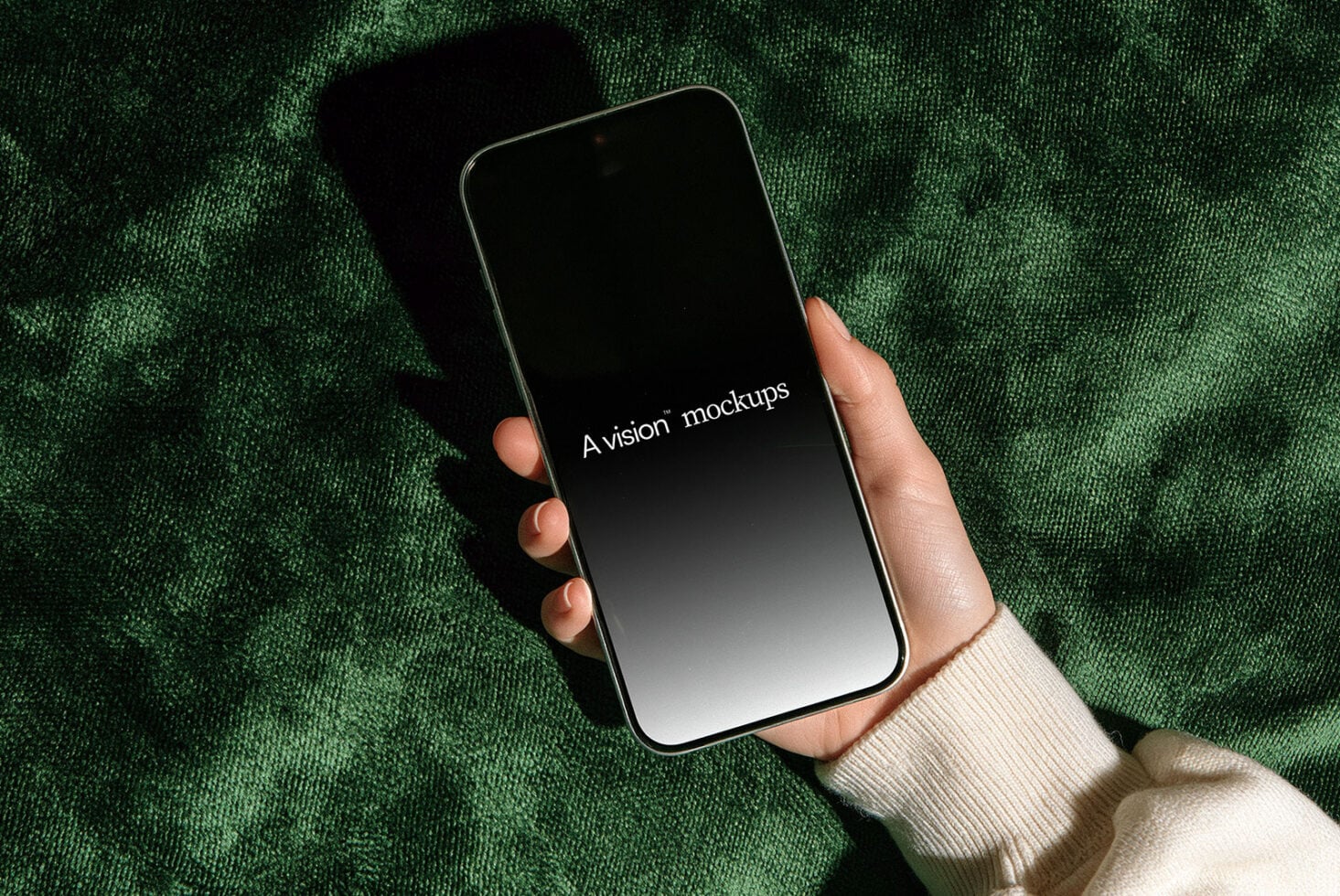 Hand holding phone with black screen on green textured background with natural shadow