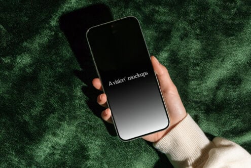 Hand holding phone with black screen on green textured background with natural shadow