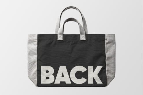 Black canvas tote bag mockup with gray handles, bold BACK text centered on front