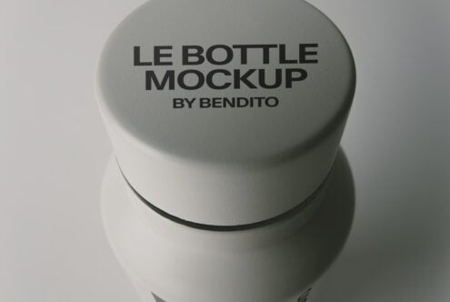 Minimal cylindrical bottle with sage green cap showing embossed text, overhead view on neutral backdrop