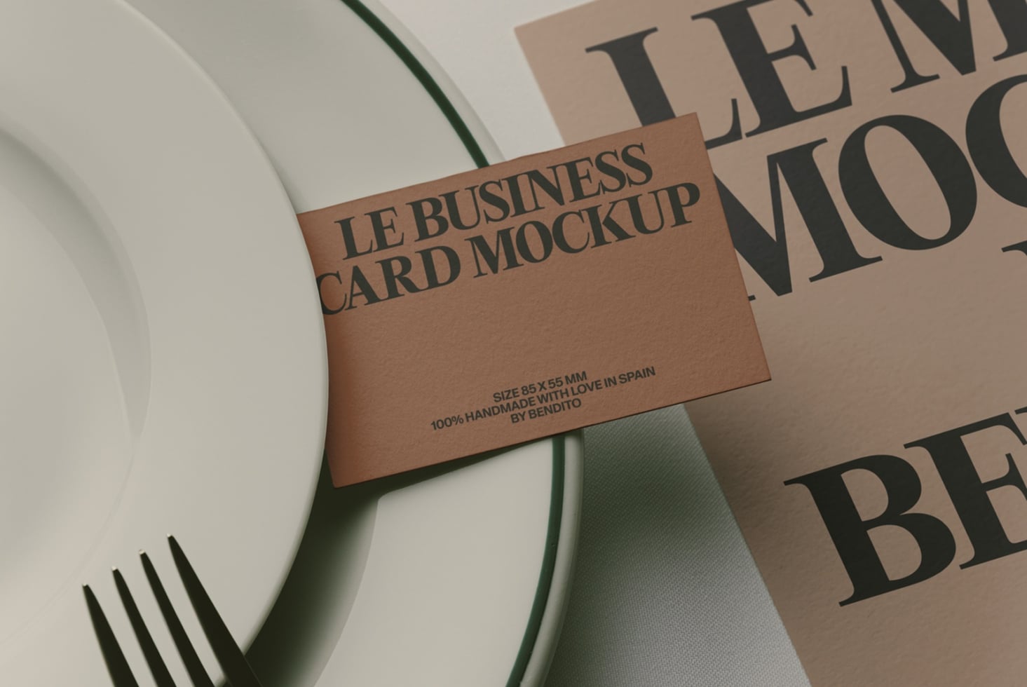 Tan business card mockup with serif typography, styled with magazines, fork, plus green plant stem on white surface