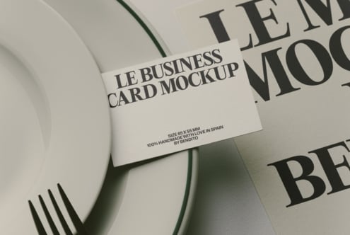Business card mockup laying on curved white surface with magazine pages behind it