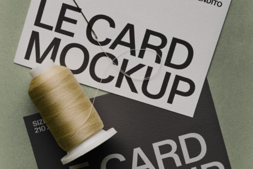 Stacked business cards with bold typography, wooden spool of thread on sage background
