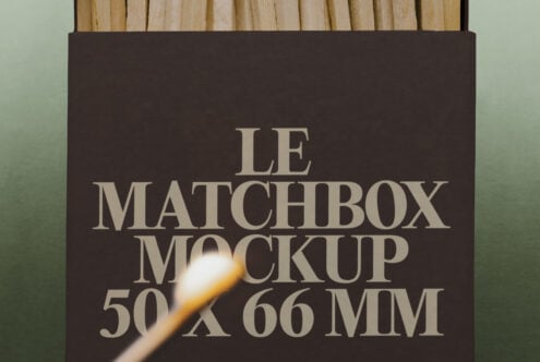 Matchbox mockup with cream serif type on dark brown box, lit match overhead, wooden surface background