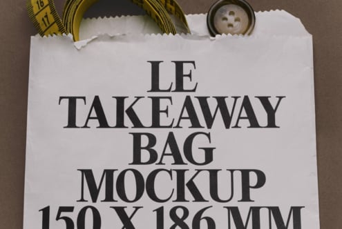 Flat lay of white paper takeaway bag with serif text, measuring tape, button, styled on brown background