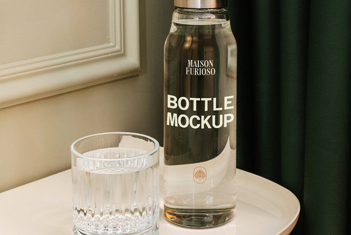 Luxury glass bottle with metal cap next to crystal tumbler on marble table, muted interior backdrop