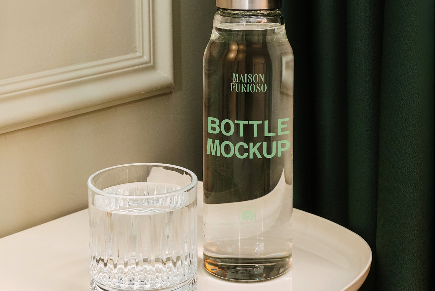 Glass bottle with mint label next to crystal tumbler on cream table, moody green backdrop
