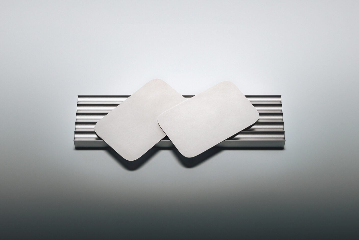 Two blank rounded square coasters on metallic striped holder with soft shadows