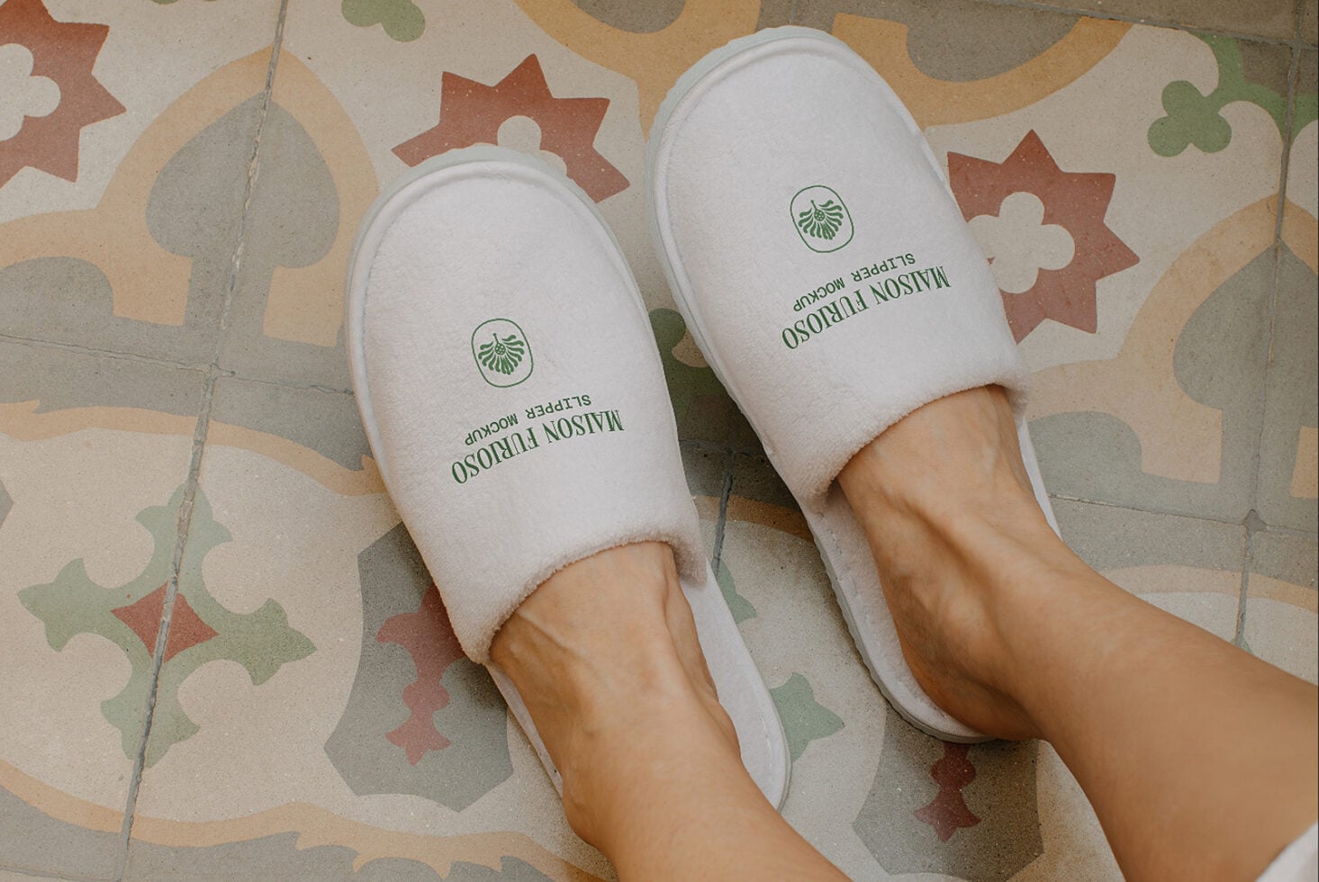 White spa slippers with green logo on patterned tile floor, feet shot overhead
