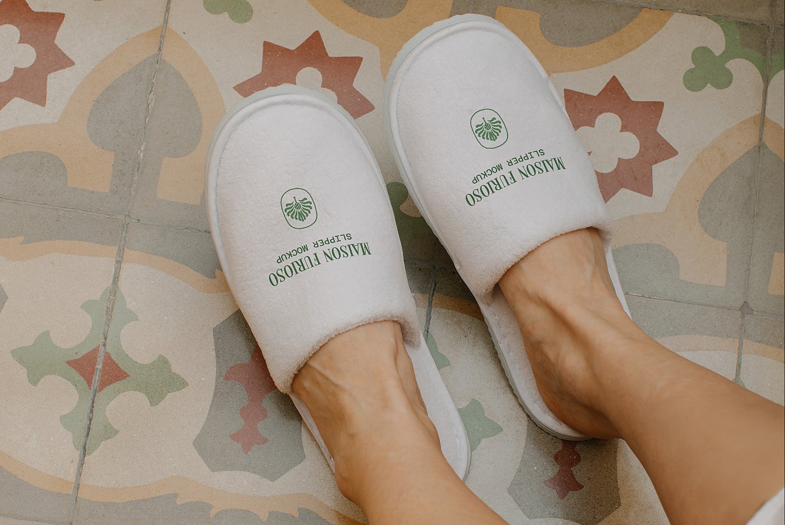 Pair of white spa slippers with green logo on colorful geometric tile floor