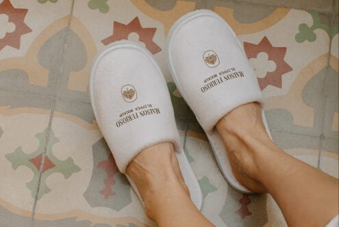 Overhead shot of white hotel slippers with gold shell logo on colorful tile floor