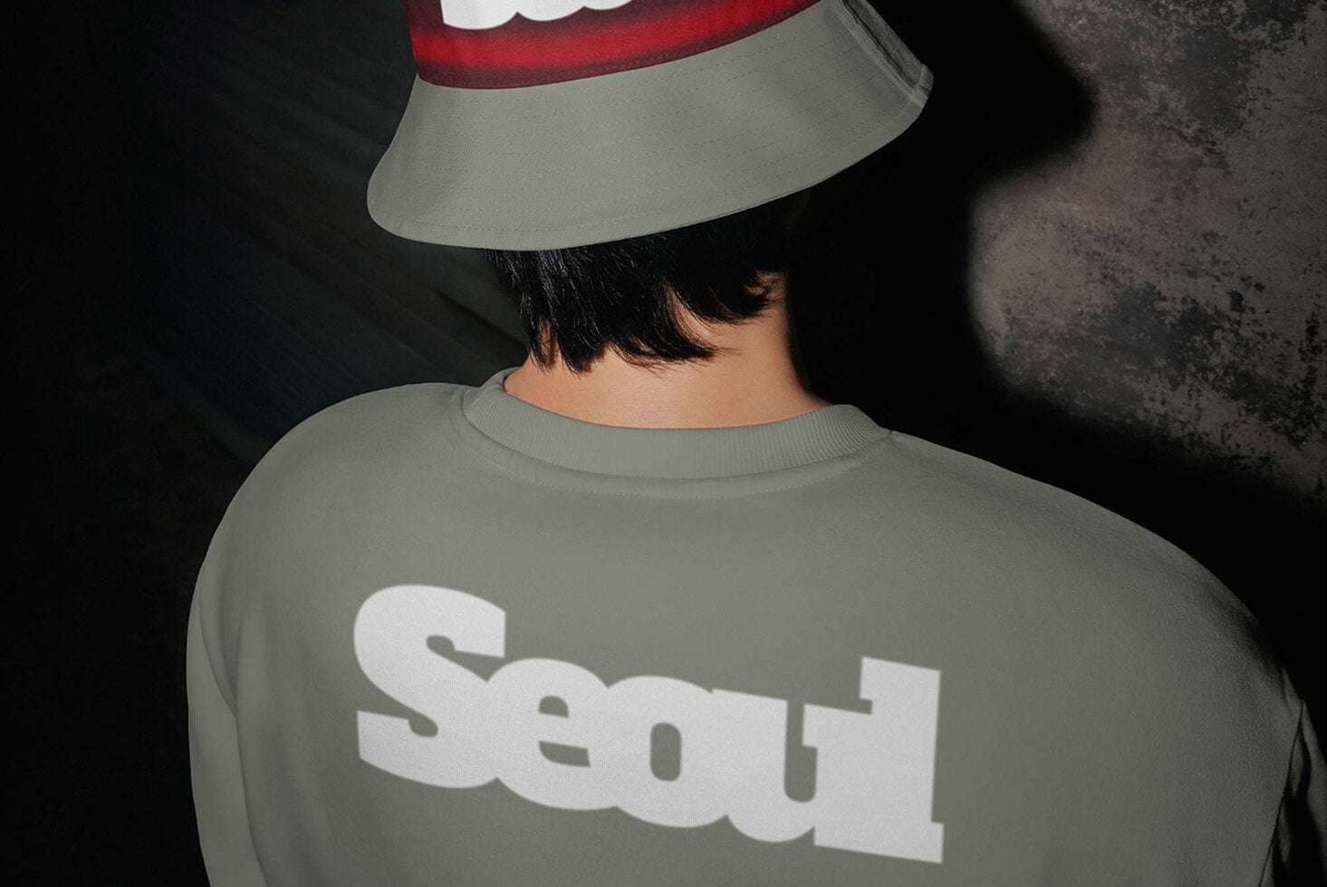 Person wearing sage sweatshirt with bold white text, red white bucket hat, dark textured background