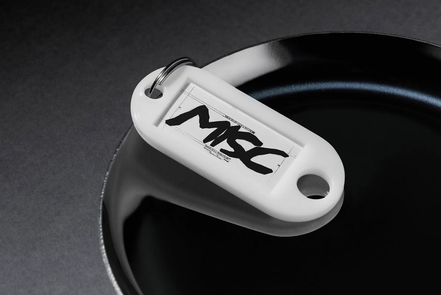 White keychain tag mockup with bold black brush lettering on dark background