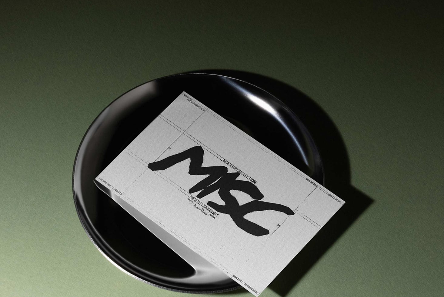 Folded leaflet with bold black typography resting on a dark circular tray against sage green background