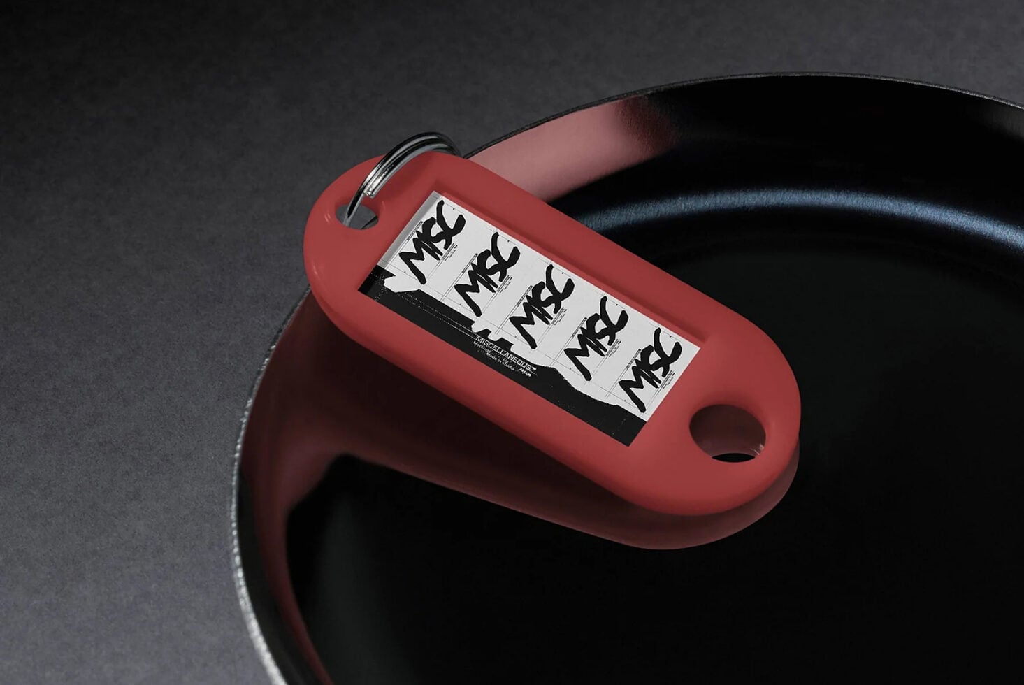 Red keychain tag mockup with black label strip showing repeated text on dark surface