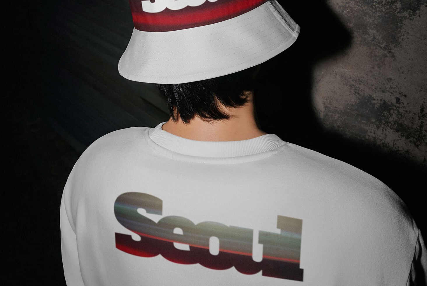 Person wearing white crewneck sweatshirt with red graphic, matching white visor, shot from behind