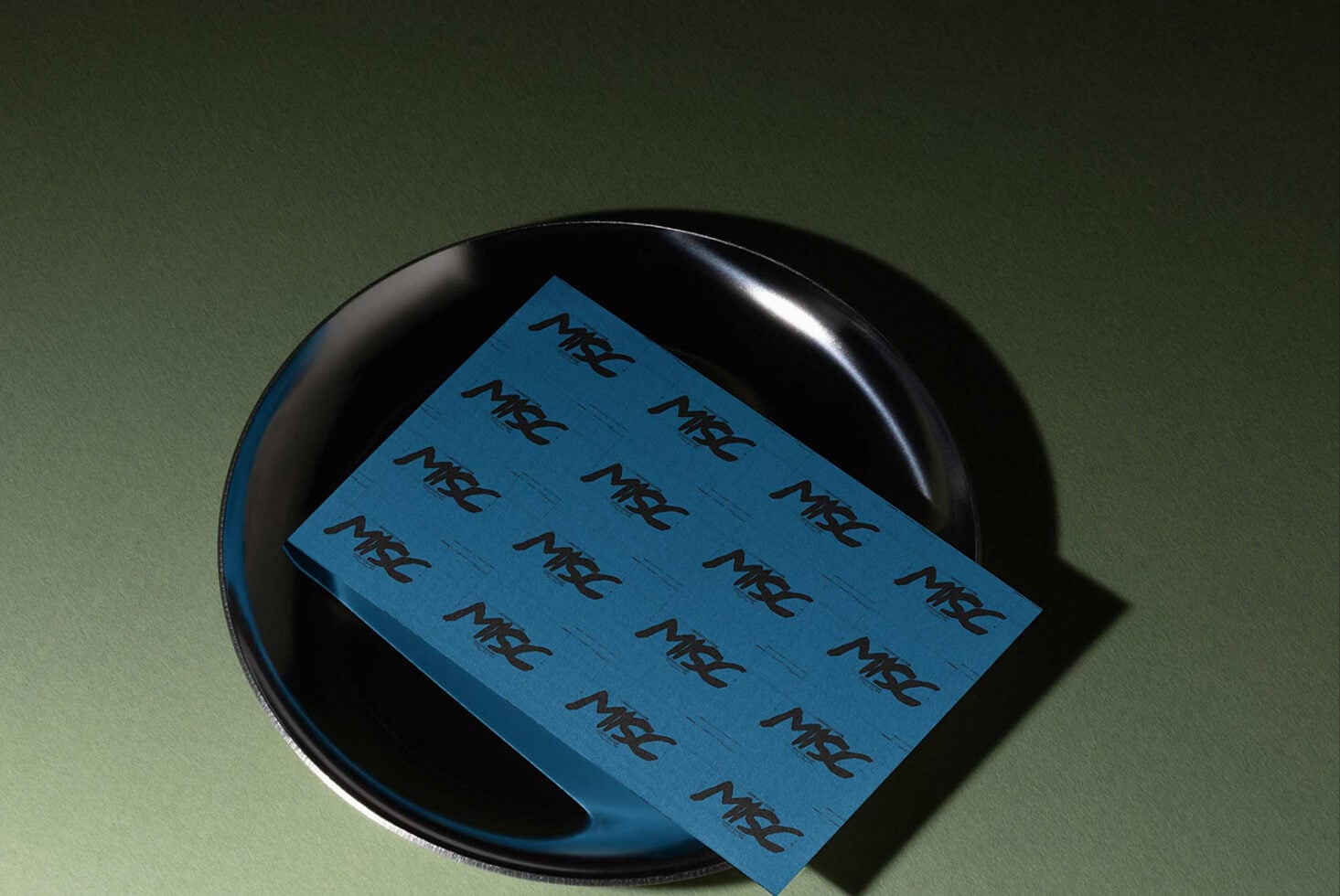 Blue business card mockup draped over black circular object with sage green background