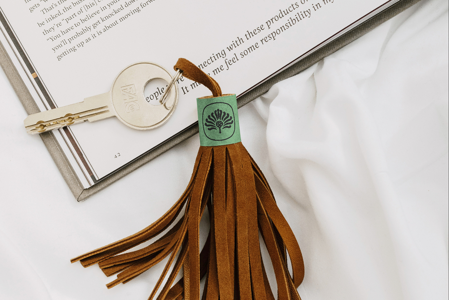 Leather tassel keychain with green label lying on open book next to vintage key