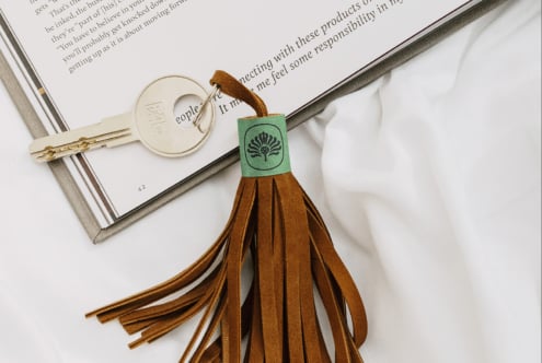 Leather tassel keychain with green label lying on open book next to vintage key