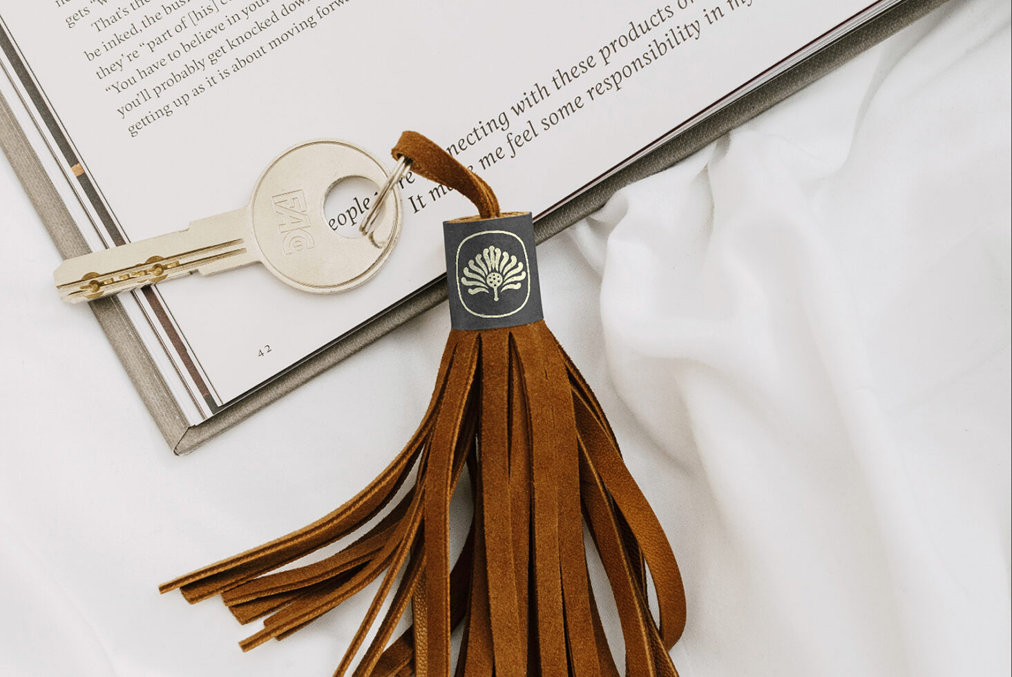 Styled flat lay with open book, cream key, brown leather tassel keychain with shell logo