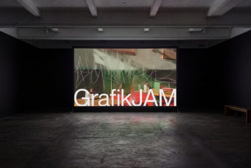 Large projection screen mockup in industrial gallery space showing GrafikJAM text with abstract overlay