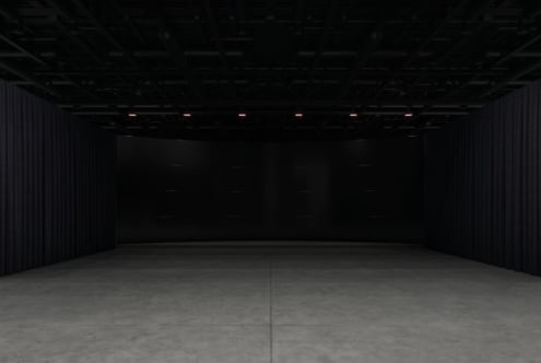 Empty warehouse studio with concrete floor, black curtains, industrial ceiling