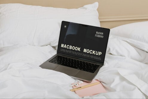 MacBook on white bedding with notebook, pencils, minimal aesthetic styling