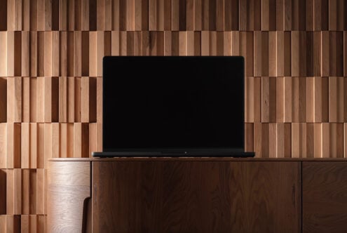 Laptop mockup on wood desk against geometric wood slat wall background