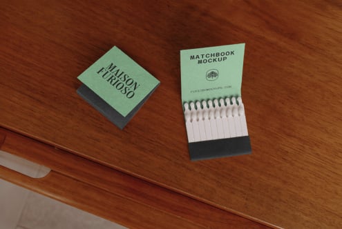 Matchbook mockup with sage green cover, white matches visible inside, styled on warm wood surface