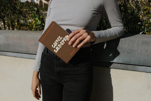 Person in gray long sleeve holding brown book mockup with white typography outdoors