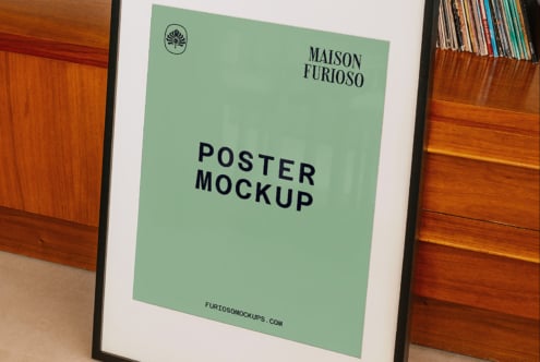 Sage green poster mockup in black frame leaning against wooden shelving with vinyl collection