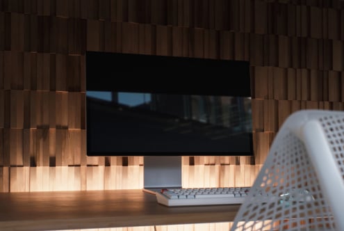 Monitor mockup on wooden desk with keyboard, warm lighting, modern workspace setup