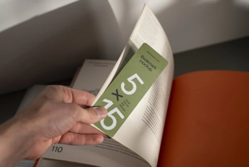 Bookmark mockup on open book page with sage green design, hand holding it in place