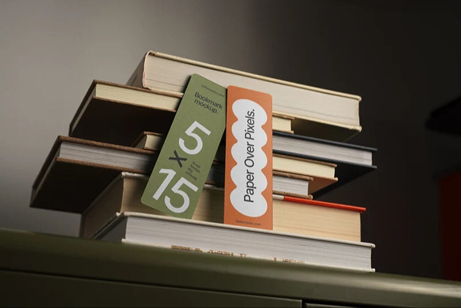 Bookmark mockup with green plus orange designs leaning on stacked books with warm lighting