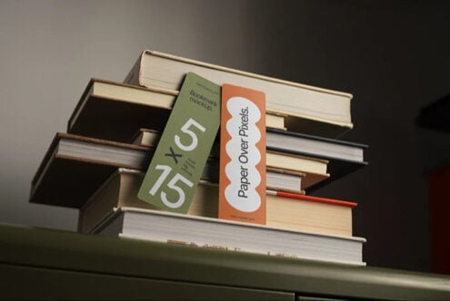 Bookmark mockup with green plus orange designs leaning on stacked books with warm lighting